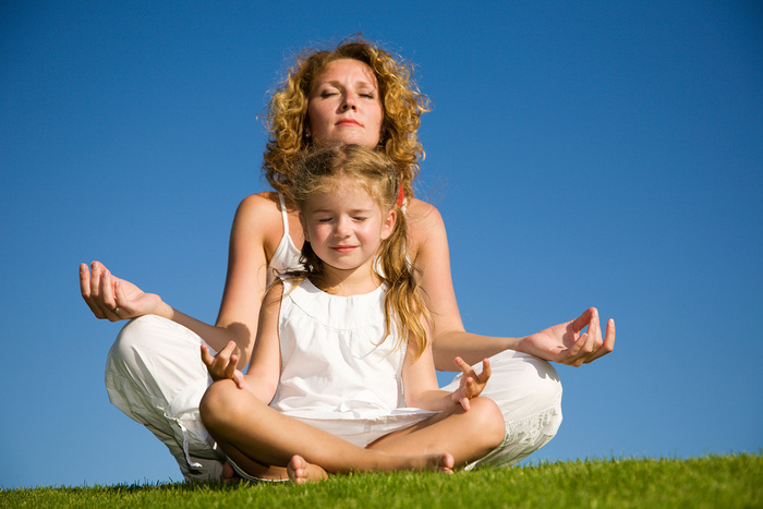 Mother and daughter sitting on grass and meditating