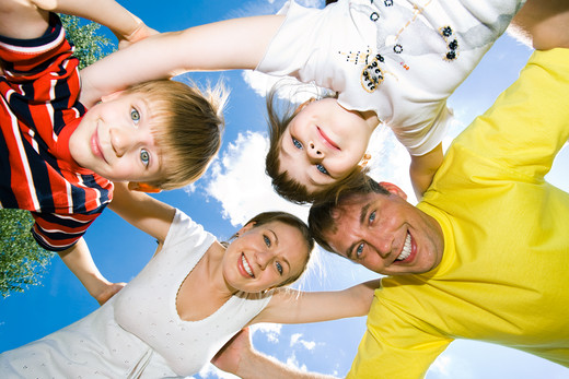 View from below of happy family embracing each other and looking at camera on the background of sky