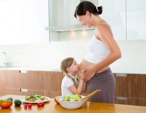 Beautiful pregnant mother with her daughter at kitchen