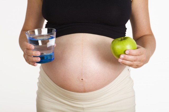 Pregnant woman holding a glass of water and a green apple.