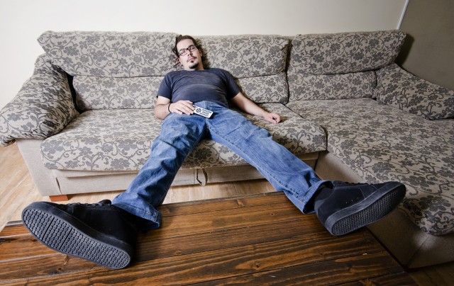 Adult man resting in sofa like a couch potato with remote control on belly