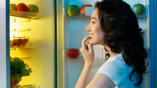 Женщина заглядывает в холодильник с едой